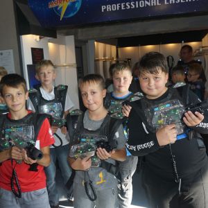 Grupa chłopców w laser game ubranych w kamizelki i trzymających w dłoniach laserowe pistolety.