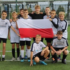 Grupa chłopców stojąca na tle bramki do piłki nożnej, trzymająca w rękach flagę Polski.