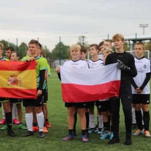Dwie drużyny chłopców stojące na boisku i trzymające w rękach flagi.