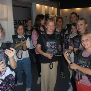 Grupa uśmiechniętych dziewczynek ubranych w czarne kamizelki i trzymająca w dłoniach laserowe pistolety.