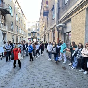 Uczniowie stojący na ulicy Piotrkowskiej. Tyłem do zdjęcia stoi przewodniczka ubrana w czerwoną kurtkę.