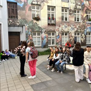 Uczniowie zadzierają głowy i podziwiają mural zamieszczony na jednym z bloków w Łodzi.