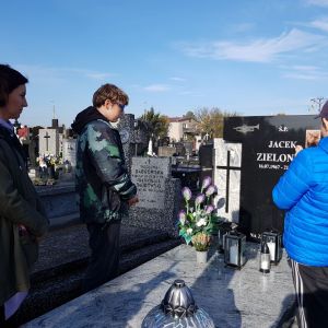 Dwóch uczniów wraz z opiekunem stoją przy grobie zmarłego nauczyciela muzyki - Jacka Zielonki