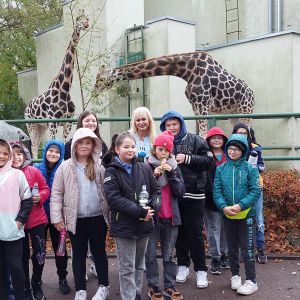 Grupa uczniów wraz z wychowawczynią, za nimi stoją dwie żyrafy.