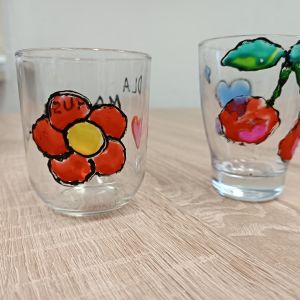 Dwie szklanki. Na jednej namalowany jest czerwony kwiatek, na drugiej dwie czerwone wisienki.