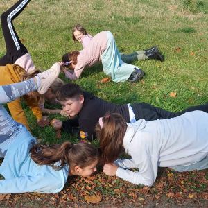 Grupa uczniów leżących i klęczących na trawie próbujących naśladować zwierzęta wodne.