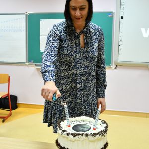 Otwórz zdjęcie - kobieta kroi tort na którym znajduje się logo szkoły.