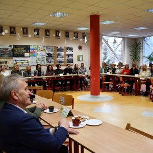 Otwórz zdjęcie - grupa osób różnej płci siedząca w ławkach ustawionych w literę "u".
