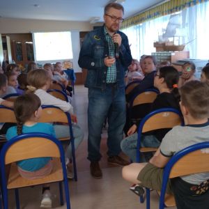 Otwórz zdjęcie - pisarz chodzący pośród uczniów, odpowiadający na ich pytania.