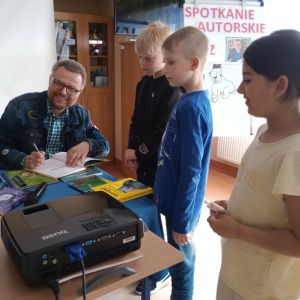 Otwórz zdjęcie - Marcin Kozioł wpisuje dedykację do zakupionych przez uczniów książek.