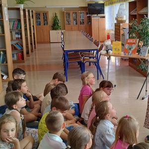 Otwórz zdjęcie - Mama jednej z uczennic czyta książkę dzieciom siedzącym na dywanie.