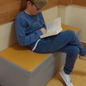 Otwórz zdjęcie - Uczeń siedzący na pufie i czytający książkę.