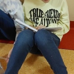 Otwórz zdjęcie - Uczennica siedząca pod ścianą czytająca książkę.