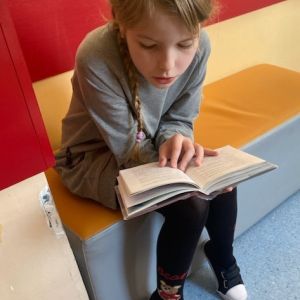 Otwórz zdjęcie - Uczennica siedząca na pufie czytająca książkę.