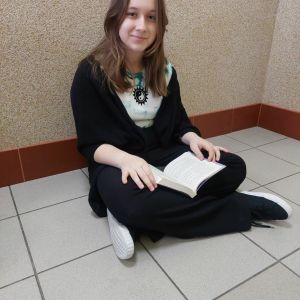 Otwórz zdjęcie - Uczennica siedząca po turecku pod ścianą czytająca książkę.
