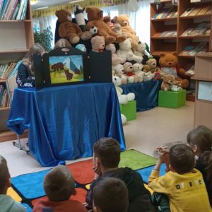 Otwórz zdjęcie: Uczniowie siedzą na dywanie i słuchają czytanego przez siódmoklasistów teatrzyku.