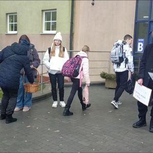 Otwórz zdjęcie - Wolontariusze rozdają cukierki wchodzącym do szkoły osobom.