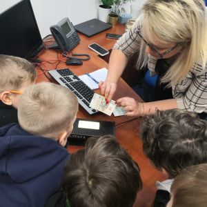 Otwórz zdjęcie - Uczniowie kładą banknot na maszynce i sprawdzają jego autentyczność.