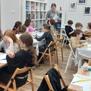 Otwórz zdjęcie - Prowadząca warsztaty wyjaśnia uczniom w jaki sposób należy obchodzić się z piórem i kałamarzem