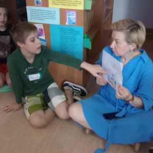 Otwórz zdjęcie - Chłopiec siedzący na podłodze po turecku opowiada o tym co narysował na kartce.