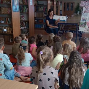 Otwórz zdjęcie - Siedząca na krześle mama jednej z uczennic czyta książkę pozostałym uczniom siedzącym na dywanie.