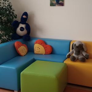 Otwórz zdjęcie - Kolorowa kanapa narożna a przy niej kwadratowy stolik. Na kanapie leżą maskotki.