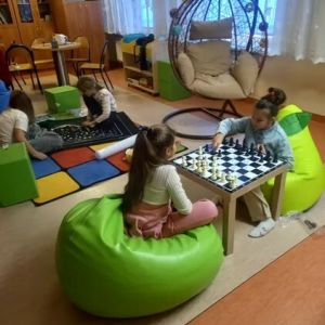 Otwórz zdjęcie - Na pierwszym planie na fotelach sako siedzą dwie uczennice grające w warcaby.