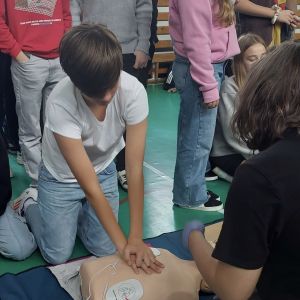 Otwórz zdjęcie - Uczeń klęcząc przed fantomem uczy się odpowiedniego uciskania klatki piersiowej.