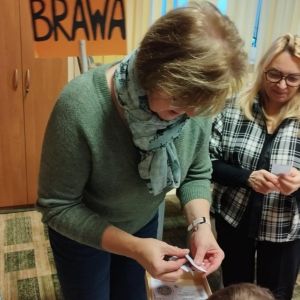 Otwórz zdjęcie - Pani dyrektor pochyla się nad kartką z zadaniami z tabliczki mnożenia.