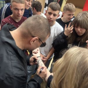 Otwórz zdjęcie - Rymcerze rozdają autografy - podpisują  ręce uczniów po swoim występie.