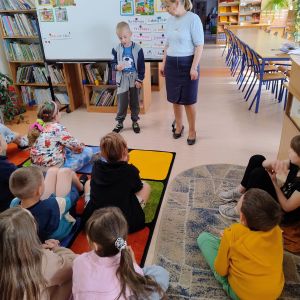 Otwórz zdjęcie - Chłopiec stojący po środku biblioteki czyta prośby książki, jakie kieruje ona do dzieci.