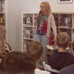 Otwórz zdjęcie - autorka książek, Joanna Jagiełło trzyma w dłoni mikrofon i opowiada o swoich książkach.