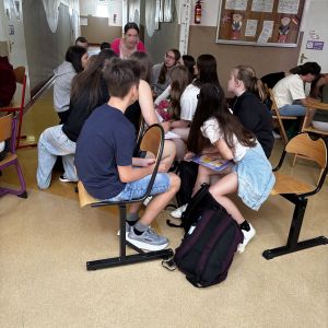 Otwórz zdjęcie - Duża grupa uczniów dyskutuje w kręgu na szkolnym korytarzu