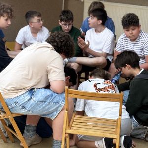 Otwórz zdjęcie - Grupa chłopców siedzi w kole, jeden z nich żywo gestykuluje, tłumacząc coś reszcie