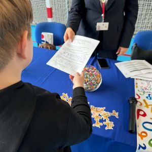Otwórz zdjęcie - Zbliżenie na ucznia oddającego kartę odpowiedzi kobiecie stojącej przy stole.