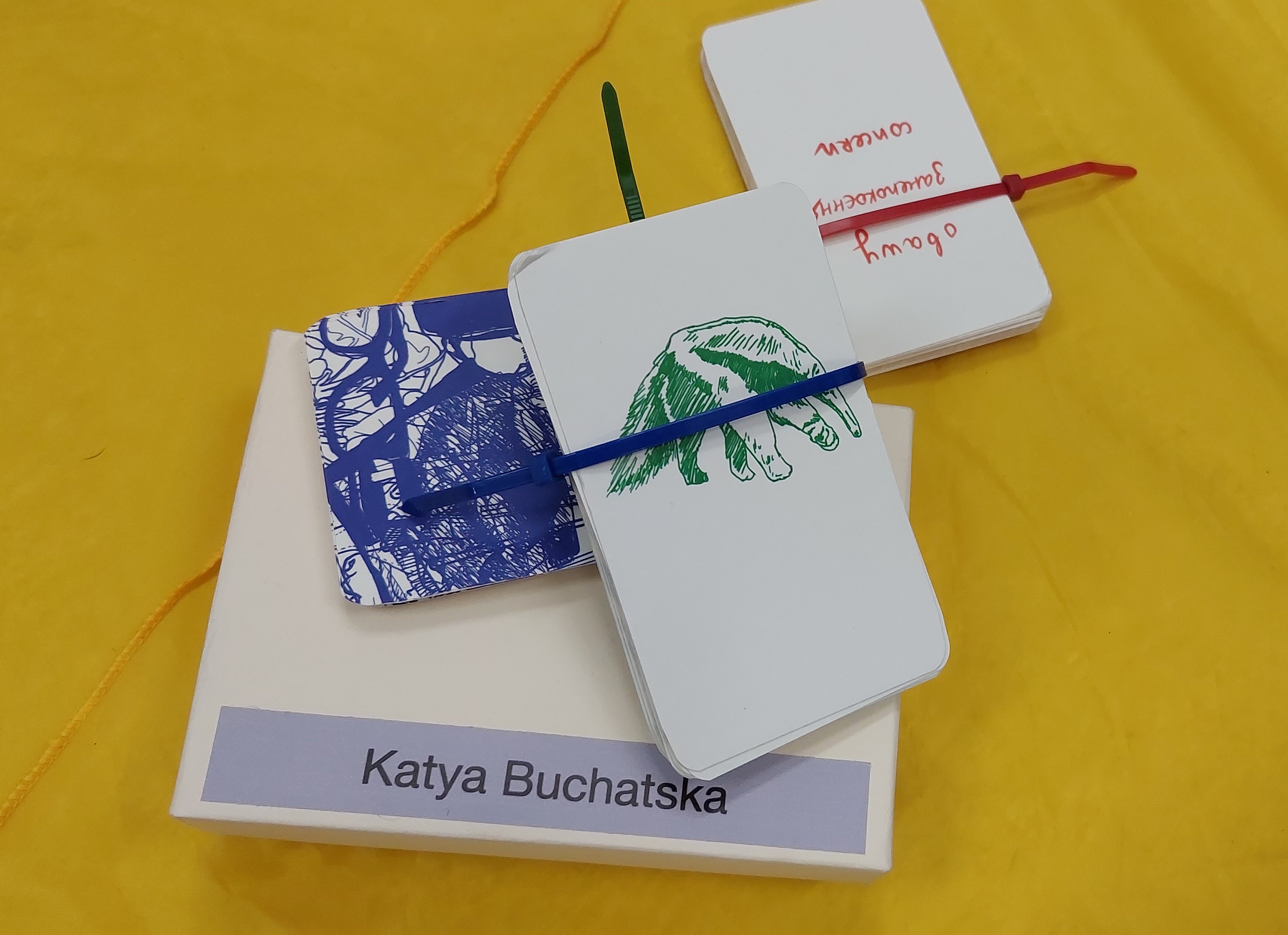 Karty autorstwa Katyi Buchatskiej leżące na żółtej chuście.