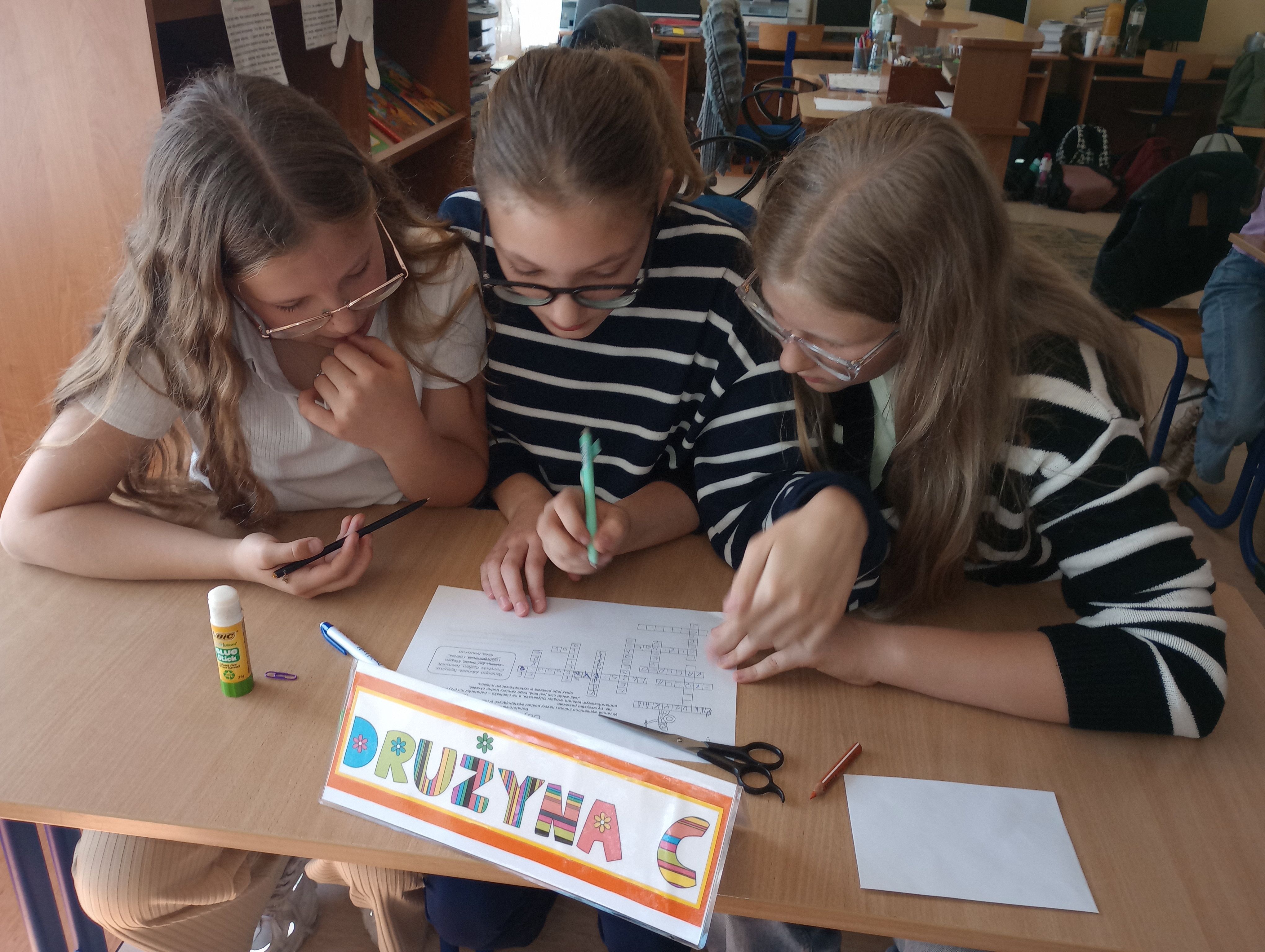 Dziewczynki z klasy piątej uzupełniają długopisem krzyżówkę leżącą na ławce.
